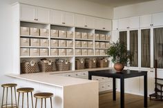 a kitchen with white cabinets and lots of baskets on the counter top next to two stools