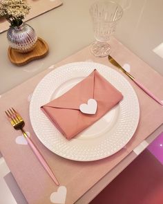 a place setting with pink napkins and hearts on the plate, along with silverware