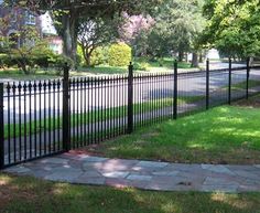 a black iron fence in the middle of a grassy area next to a sidewalk and trees