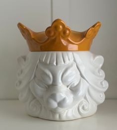 a white ceramic vase with a gold crown on it's head, sitting on a table