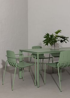 a green table with four chairs and a potted plant on the top, against a white wall