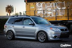 a silver subarunt is parked in front of a train with graffiti on it