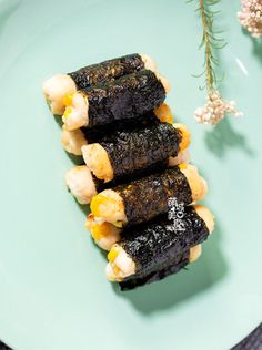 three pieces of sushi on a green plate next to some small flowers and herbs