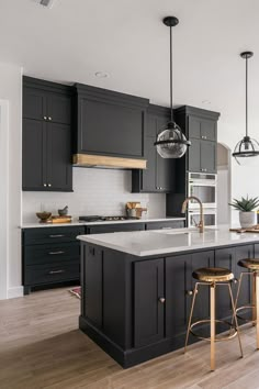 a large kitchen with black cabinets and white counter tops, gold bar stools and pendant lights hanging from the ceiling