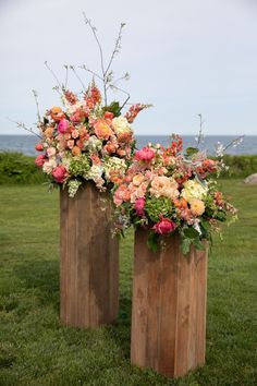 two wooden vases filled with flowers sitting on top of a lush green field next to the ocean