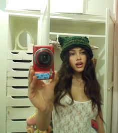 a woman taking a selfie in front of a mirror with a camera and hat on