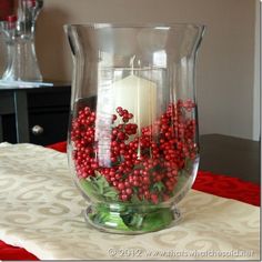 a glass vase filled with red berries and a lit candle sitting on top of a table