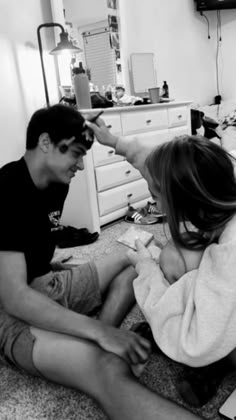 a man and woman sitting on the floor in front of a laptop computer, one is combing the other's hair