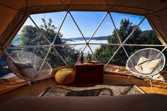 the inside of a tent with two chairs and a table in front of it, looking out onto a body of water