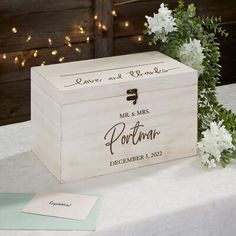 a wooden box sitting on top of a table next to white flowers and greenery