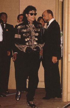 two men standing next to each other in front of a group of people wearing suits and ties