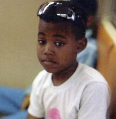 a young boy wearing sunglasses and holding a tennis racquet in his right hand