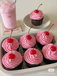 cupcakes with pink frosting and cherries on a tray next to a drink