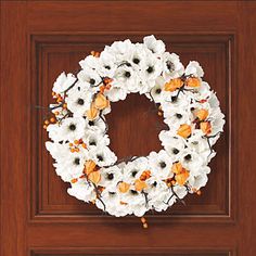 a white wreath with orange and white flowers on a wooden door