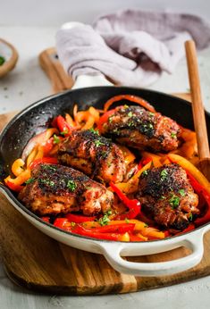 chicken and peppers in a skillet on a cutting board with wooden utensils