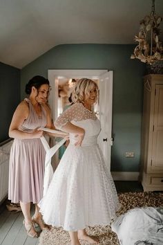 two women standing in a room with one woman wearing a wedding dress and the other holding a white ribbon