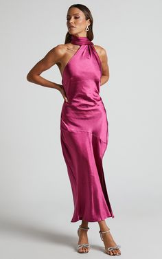 a woman wearing a pink dress with high neck and side slits, standing in front of a white background