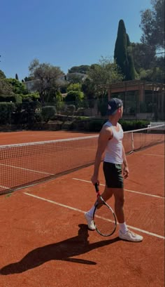 a man holding a tennis racquet on top of a tennis court with trees in the background