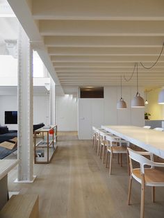 a long table and chairs in a room with white walls, wood flooring and large windows