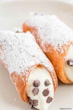 two pastries with chocolate chips and powdered sugar on them sitting on a white plate