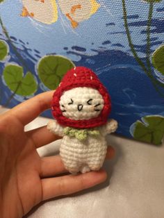 a hand holding a small crocheted cat with a red hat