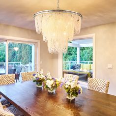 a dining room table surrounded by chairs and vases with flowers on them in front of large windows