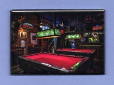 two pool tables with red cloth on them in a room filled with neon signs and video games