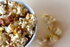 a bowl filled with popcorn and bacon on top of a white tablecloth next to a spoon