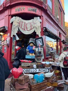 people are standing in front of a red building with many items for sale on it