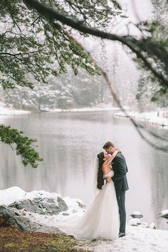 a bride and groom kissing in front of a lake during their winter wedding photo session