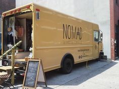 a yellow food truck parked on the side of a street next to a sidewalk with tables and chairs