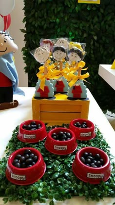 a table topped with lots of red bowls filled with black olives next to green plants