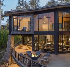 a modern house with large glass windows overlooking the trees and mountains at night, lit up by outdoor lighting