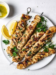 grilled chicken skewers with lemon and parsley on a white platter