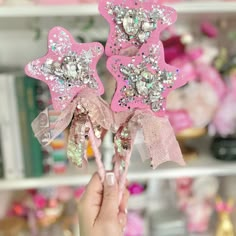 a person holding up two pink flowers with sequins on them in front of a shelf