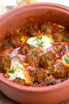 a pot filled with meatballs and sauce on top of a wooden table next to bread