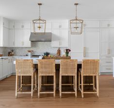 a kitchen with white cabinets and wooden chairs in front of an island table that has four hanging lights over it