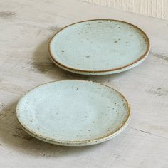 two white bowls sitting on top of a wooden table next to each other, one with brown speckles