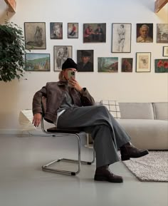 a man sitting in a chair taking a selfie with his cell phone while wearing a hat