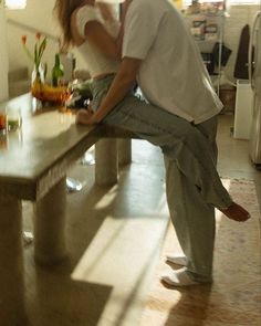 the man and woman are kissing at the table in the kitchen, with flowers on the counter