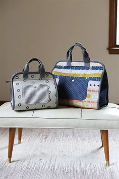 two purses sitting on top of a bench in front of a window, one is grey and the other is white