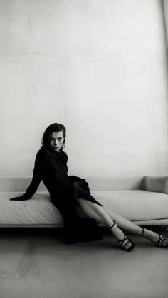 a woman sitting on top of a white couch in a black dress and high heels