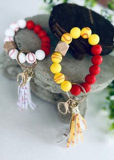 two bracelets with baseball beads and tassels are on top of a rock