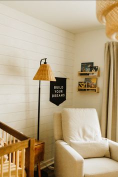 a white chair sitting next to a lamp in a living room under a sign that says build your dreams