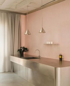 a kitchen with pink walls and stainless steel counter tops, hanging lights over the sink