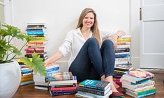 a woman sitting on the floor surrounded by stacks of books and smiling at the camera