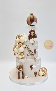 a three tiered cake decorated with gold and white balloons, teddy bears and other decorations