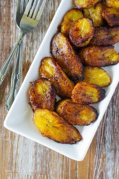 grilled bananas in a white dish with a fork and knife next to it on a wooden table