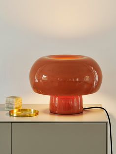 an orange lamp sitting on top of a table next to a gold object and a white wall