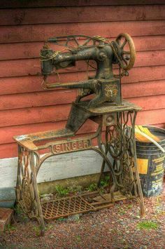 an old sewing machine sitting on top of a wooden bench next to a red building